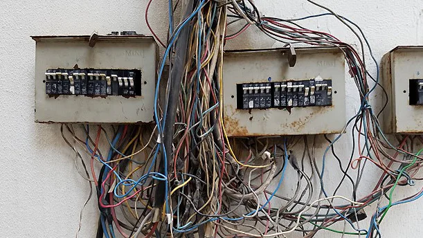 Several weathered breaker boxes surrounded by tangled electrical wiring, illustrating a physical system that grew incrementally and needed simple operational software